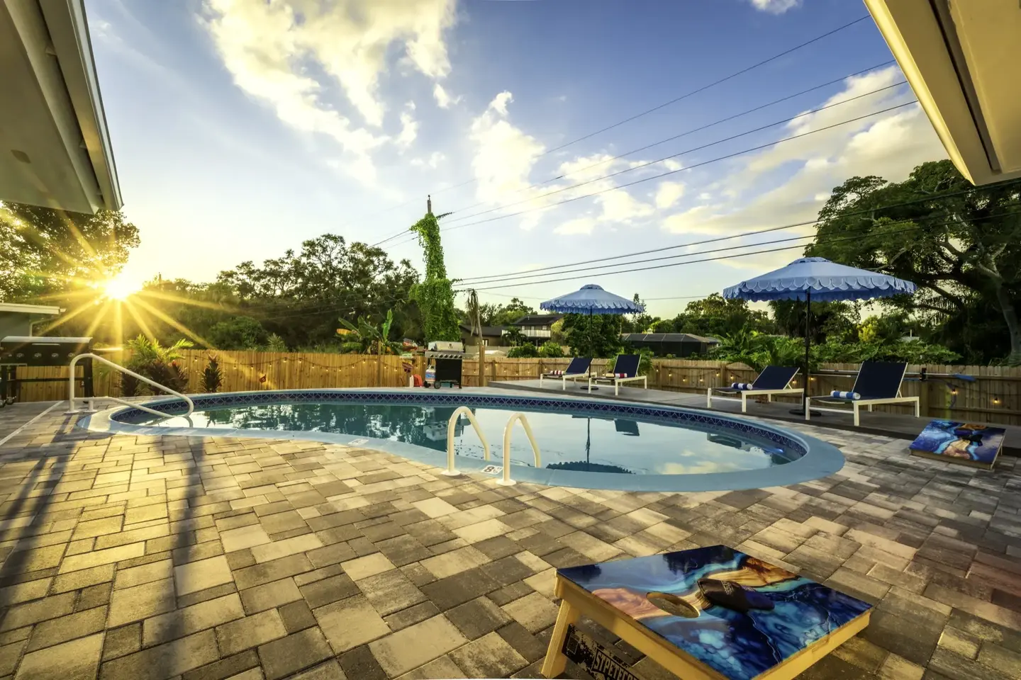 Golden-hour sunset over the pool at Chasing Vitamin Sea, with lounge chairs, beach umbrellas, and a cornhole board on the paver patio