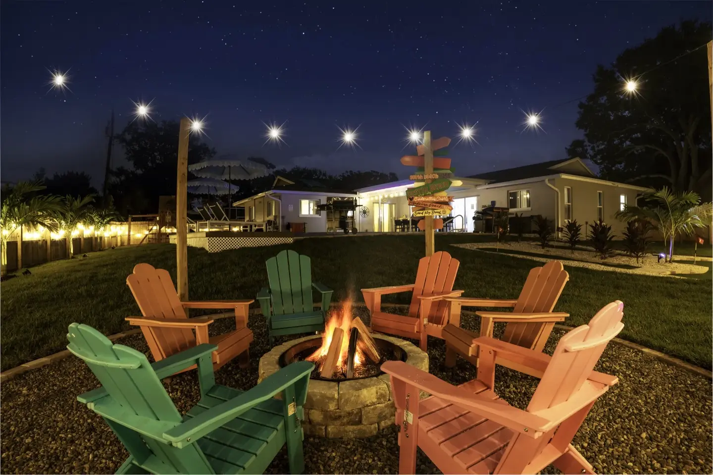 Fire pit with colorful Adirondack chairs under string lights and a starry sky at Chasing Vitamin Sea